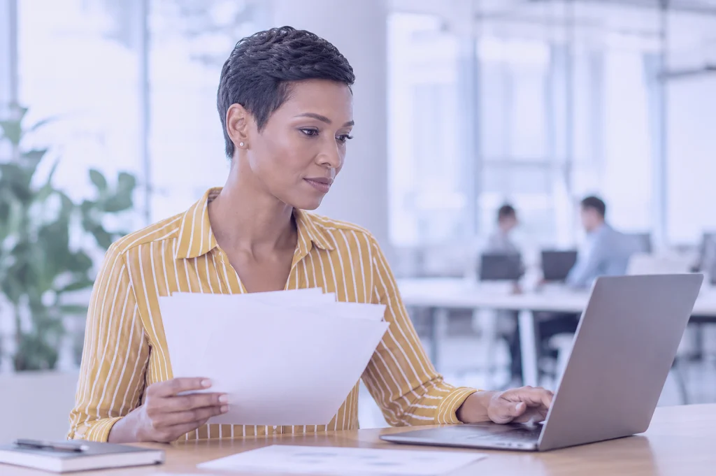 Geschäftsfrau prüft Unterlagen zur CSDDD-Compliance am Laptop in modernem Büro